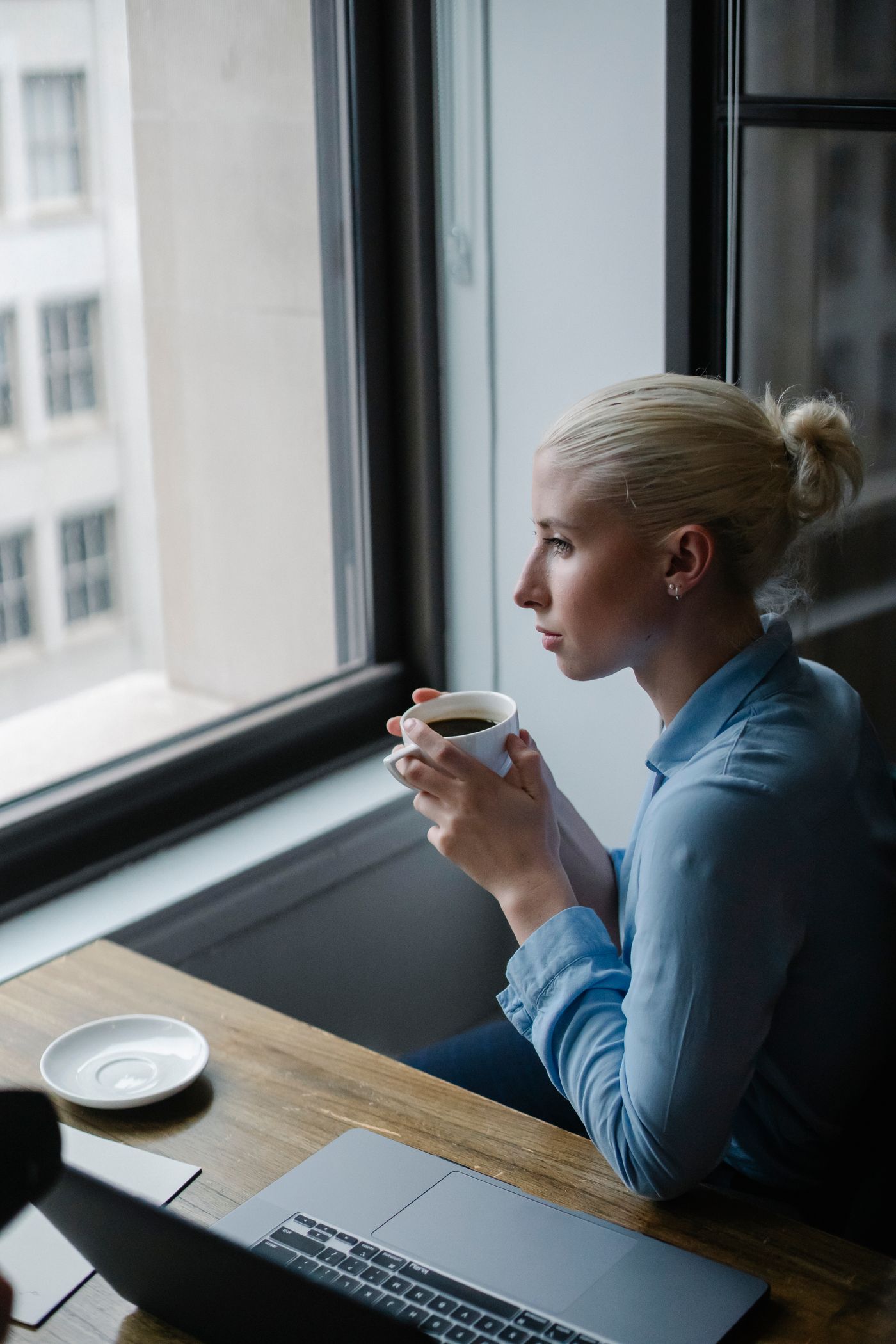 Frau steht mit einer Tasse am Fenster und macht eine Pause
